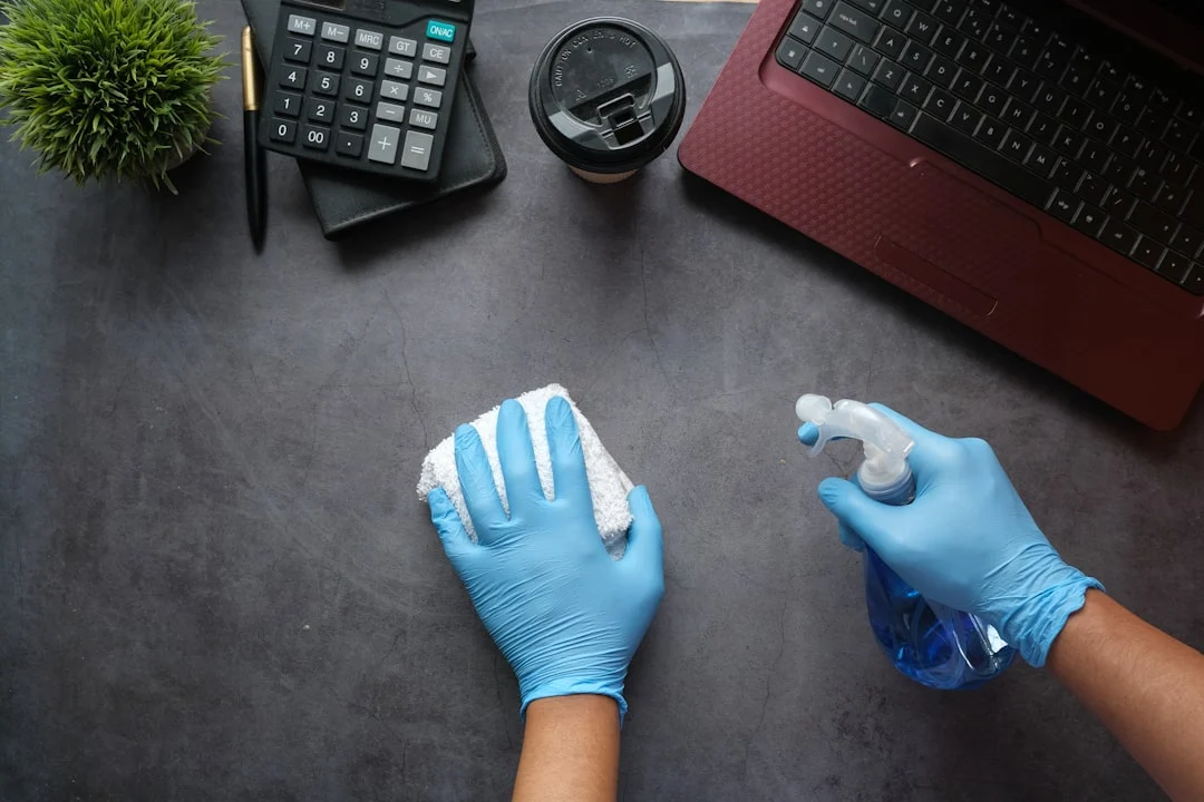 Gloved hands cleaning an office desk with a spray bottle and cloth